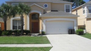 A two-story house with a garage, a front door, and a small front yard with a palm tree.