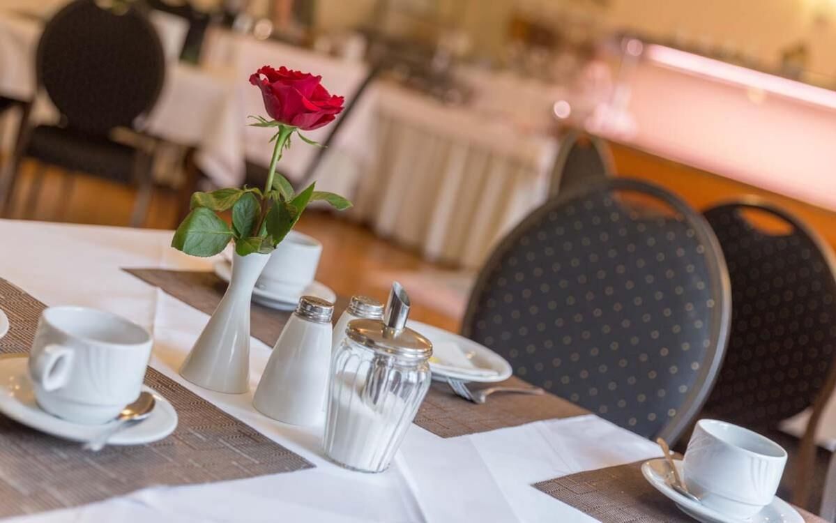 A dining table set with white tableware, a red rose, and salt and pepper shakers.