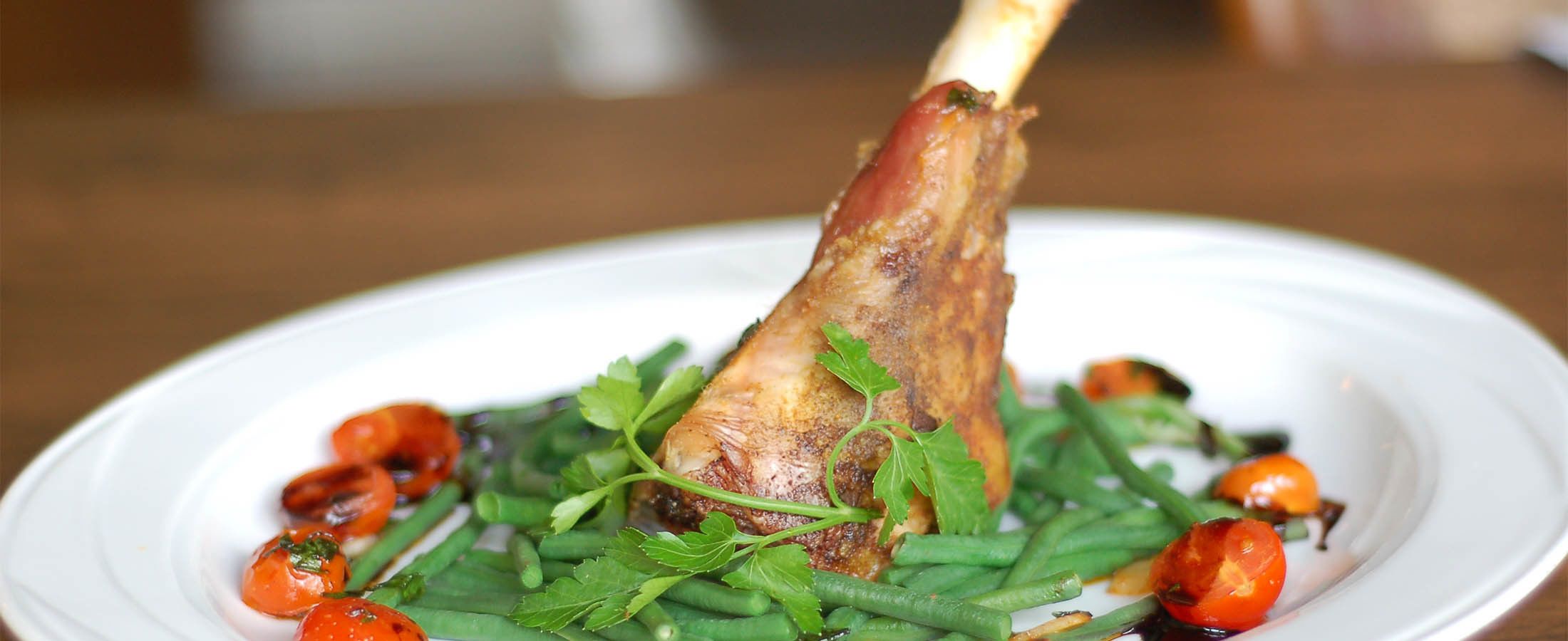Ein Teller mit gebratenem Lammkeulchen, grünen Bohnen, Kirschtomaten und Rucola.