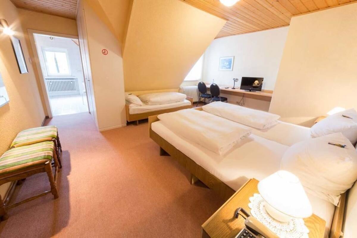 A bedroom with two single beds, a desk with a chair, a small table with a lamp, and a window.