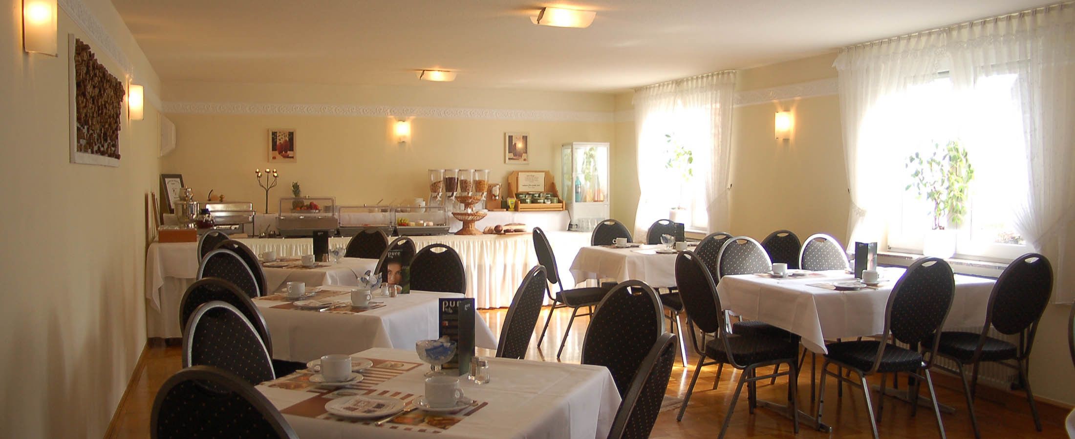 A dining area with multiple tables and chairs, a buffet setup, and a kitchen in the background.
