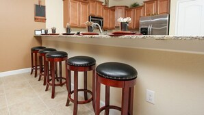 A kitchen with wooden cabinets, a stainless steel refrigerator, a sink, and four bar stools.