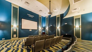 A conference room with rows of chairs, a large screen, and wall-mounted lighting.