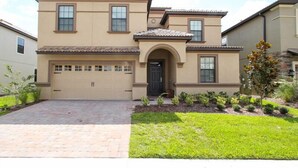 A two-story house with a garage, a front door, and a small front yard with plants.