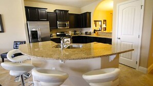 A kitchen with dark cabinets, a stainless steel refrigerator, a microwave, a sink, and a bar area with stools.