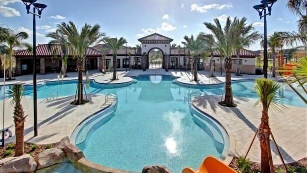 A swimming pool area with a central pool, surrounded by palm trees and a building with a red roof.