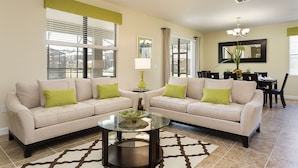A living room with two beige sofas, a glass coffee table, and a dining area with a table and chairs. - Ov3361 - Champions Gate Resort - 5 Bed 4.5 Baths Villa (Davenport)