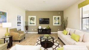 A living room with a sofa, armchairs, a coffee table, and a TV. There are two paintings on the wall and a window with blinds. - Ov3361 - Champions Gate Resort - 5 Bed 4.5 Baths Villa (Davenport)