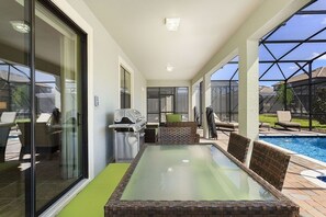Un patio coperto con un tavolo dal piano in vetro, posti a sedere all'aperto e vista su una piscina.