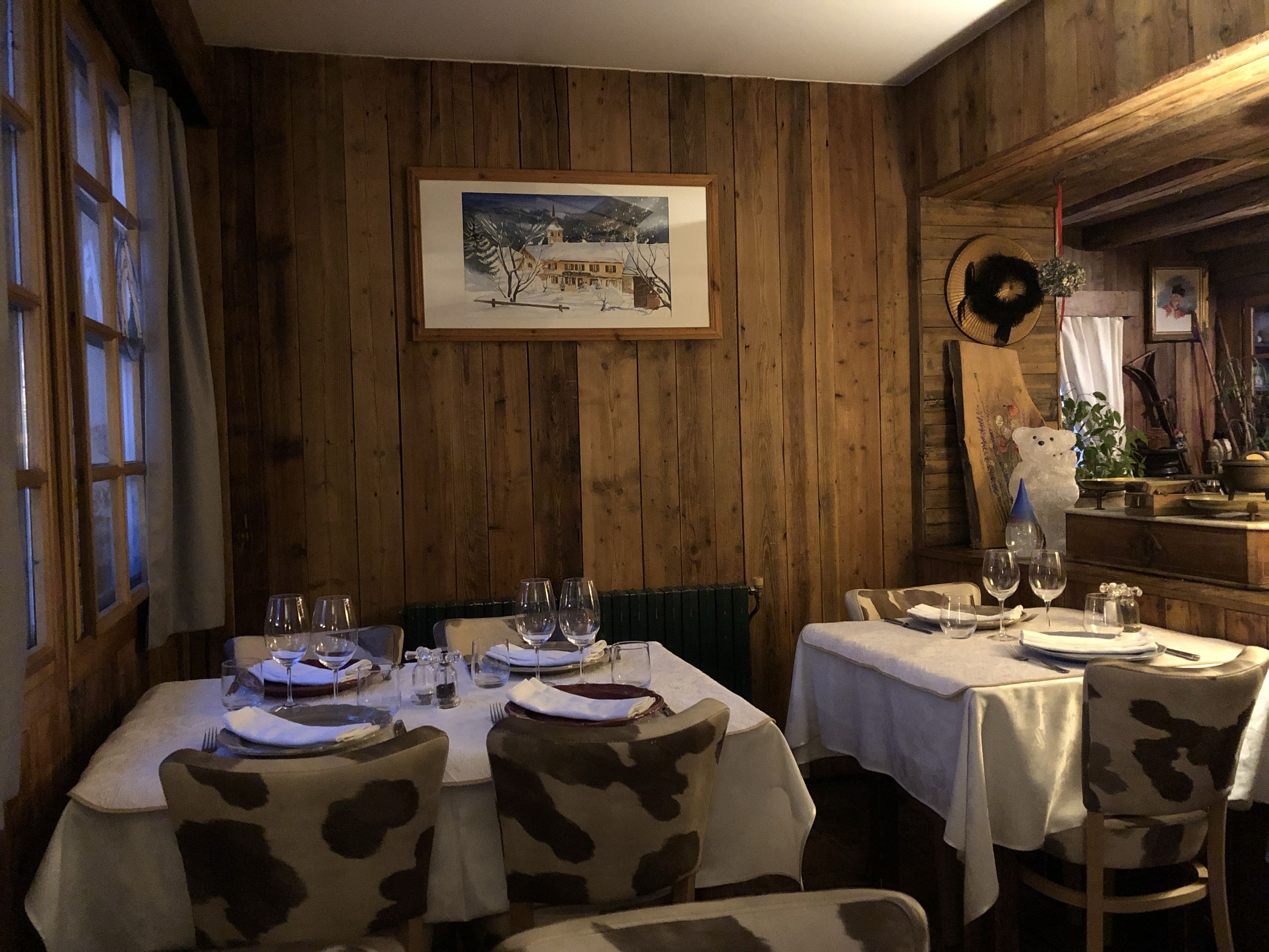 A dining area with wooden walls, a framed painting, and tables set for two with chairs.