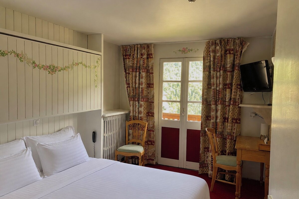 Une chambre d’hôtel avec un lit, deux chaises, un bureau, une télévision et une fenêtre avec des rideaux.