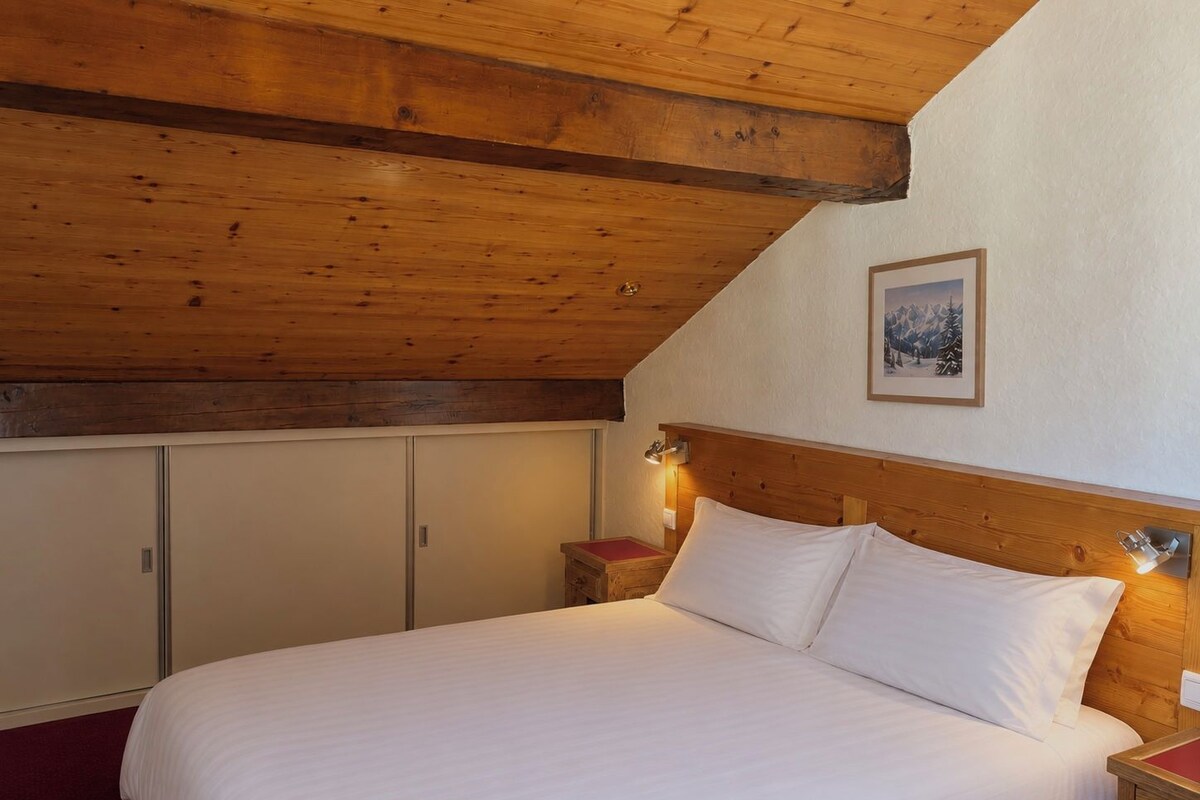 Une chambre avec un plafond en bois, un lit avec une literie blanche et une table de chevet avec une lampe.