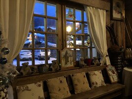 A cozy room with a wooden bench, a Christmas tree, and a window with a view of a snowy landscape.