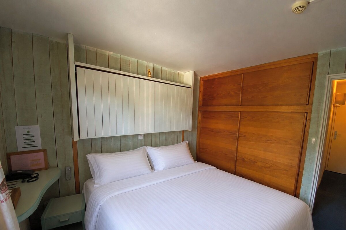 Une chambre d’hôtel avec un lit, une table de chevet, un bureau et une armoire en bois.