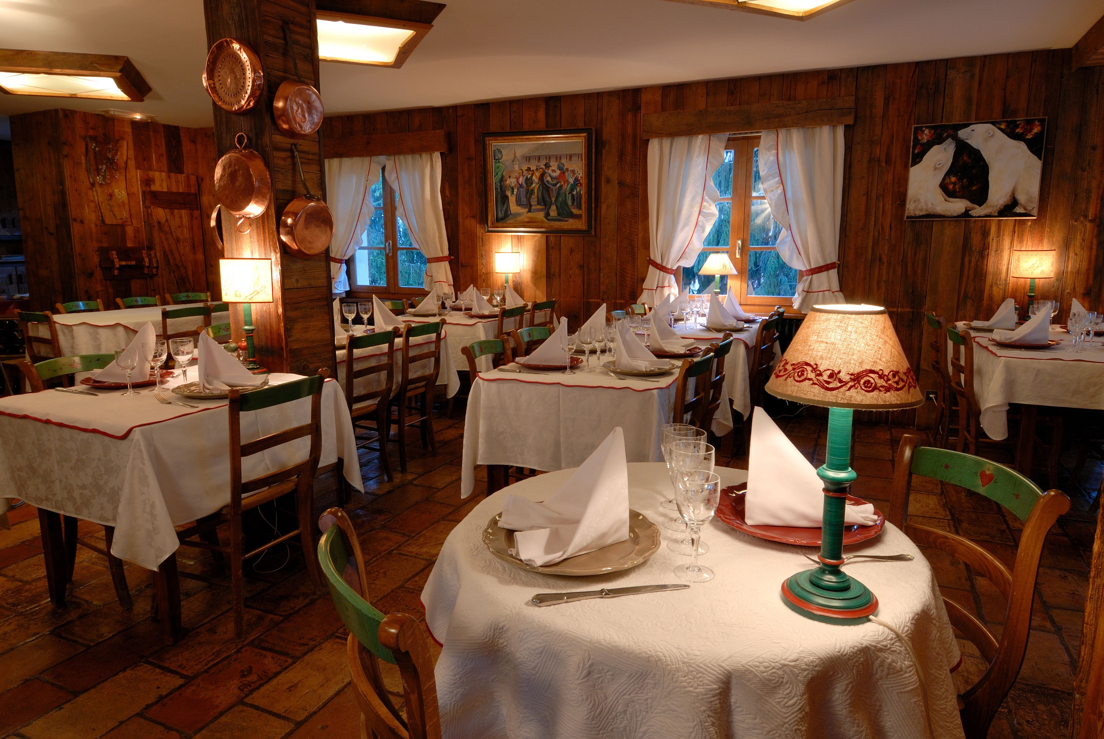 Un restaurant avec de nombreuses tables dressées pour le service, des murs en bois et une vue sur l’extérieur par les fenêtres.