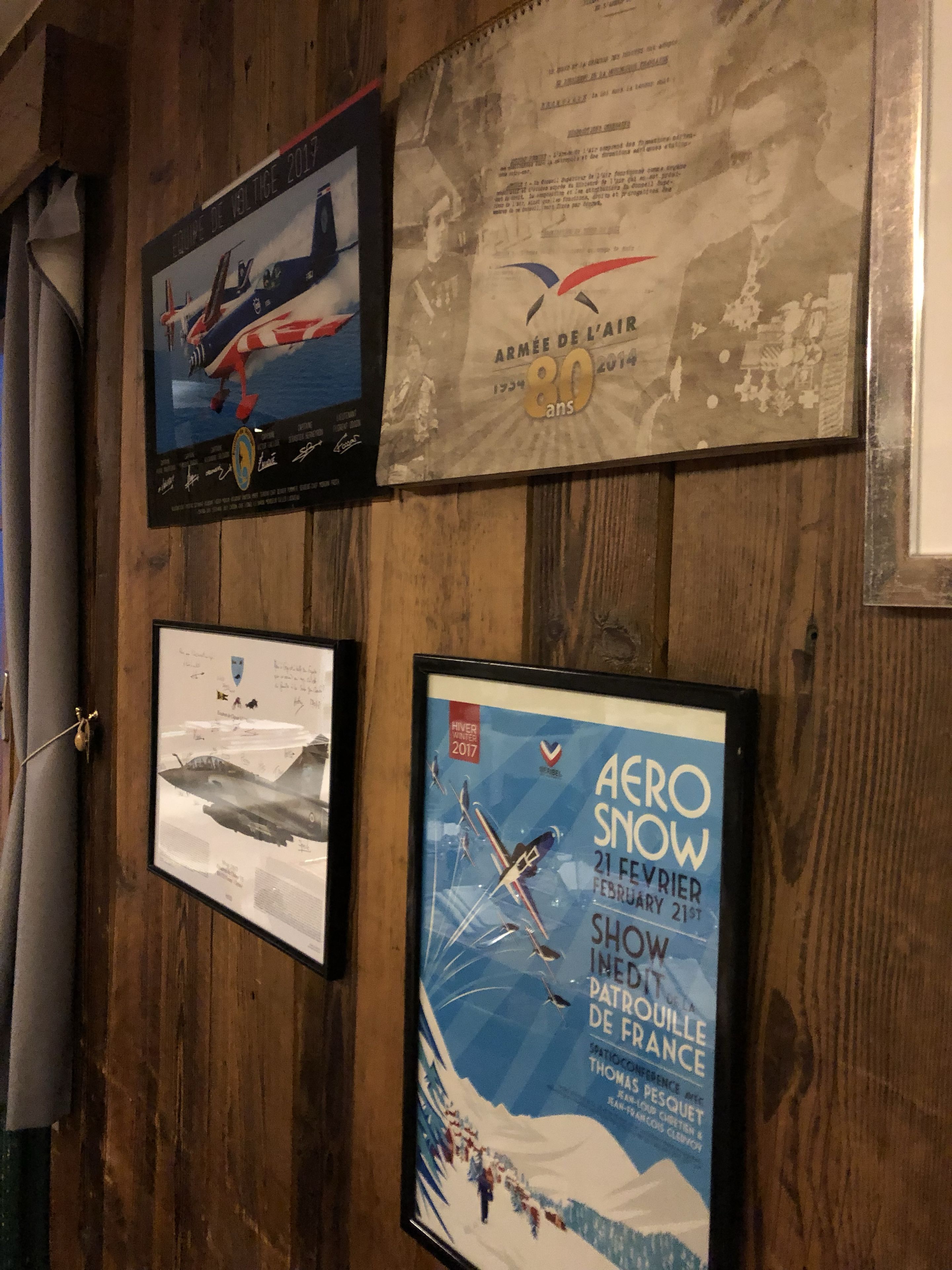 Framed posters on a wooden wall, including an airplane, a military commemoration, and an event poster.