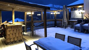 Un patio extérieur abrité, doté de meubles en bois et d’un bar, entouré d’un paysage enneigé et avec des montagnes en arrière-plan.