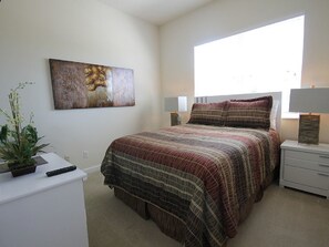 Een slaapkamer met een groot bed, een nachtkastje, een lamp, een wandeling schilderij en een potplant.