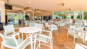 Un vaste espace de restauration intérieur, avec des tables et des chaises blanches, de grandes fenêtres et un espace central ouvert.