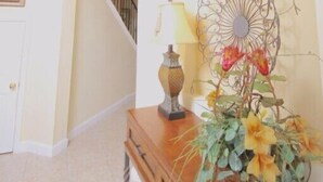 Un vaste espace de vie doté d’un haut plafond, une console en bois agrémentée d’une lampe et de fleurs, et un balcon avec une balustrade.