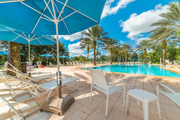 Zona junto a la piscina con sillones de descanso, sombrillas y palmeras.