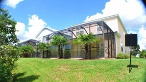 Une maison moderne dotée d’une grande extension en verre, entourée d’une pelouse bien entretenue et de palmiers.