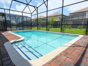 A swimming pool with a glass enclosure, surrounded by a brick patio and a view of houses.
