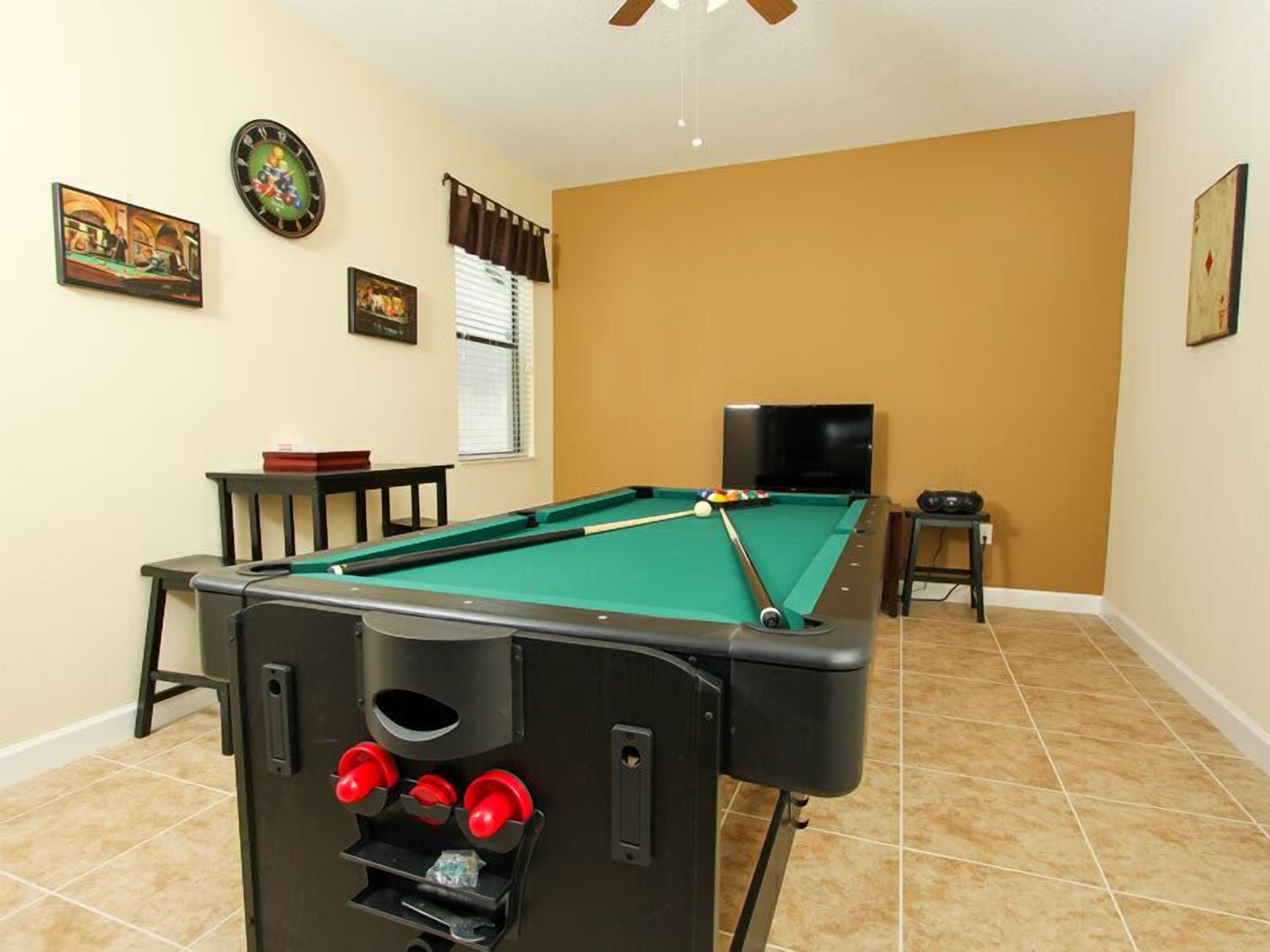 A pool table with a pool cue rack, a television, and a clock on the wall.