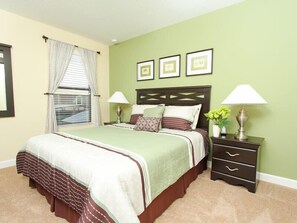 A bedroom with a bed, two bedside tables, a window with curtains, and three framed pictures on the wall.
