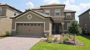 A two-story house with a beige facade, a garage, and a small front yard with landscaping. - Ov3227 - Champions Gate Resort - 5 Bed 4.5 Baths Villa (Davenport)