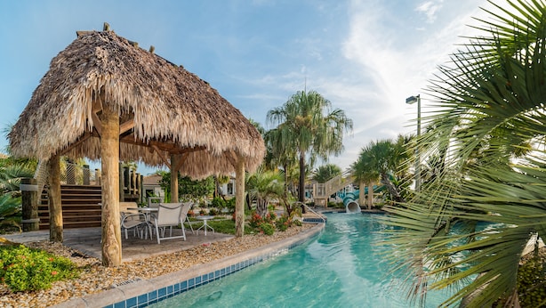 A pool area with a thatched structure, palm trees, and a tiled pool edge. - Ov3227 - Champions Gate Resort - 5 Bed 4.5 Baths Villa (Davenport)