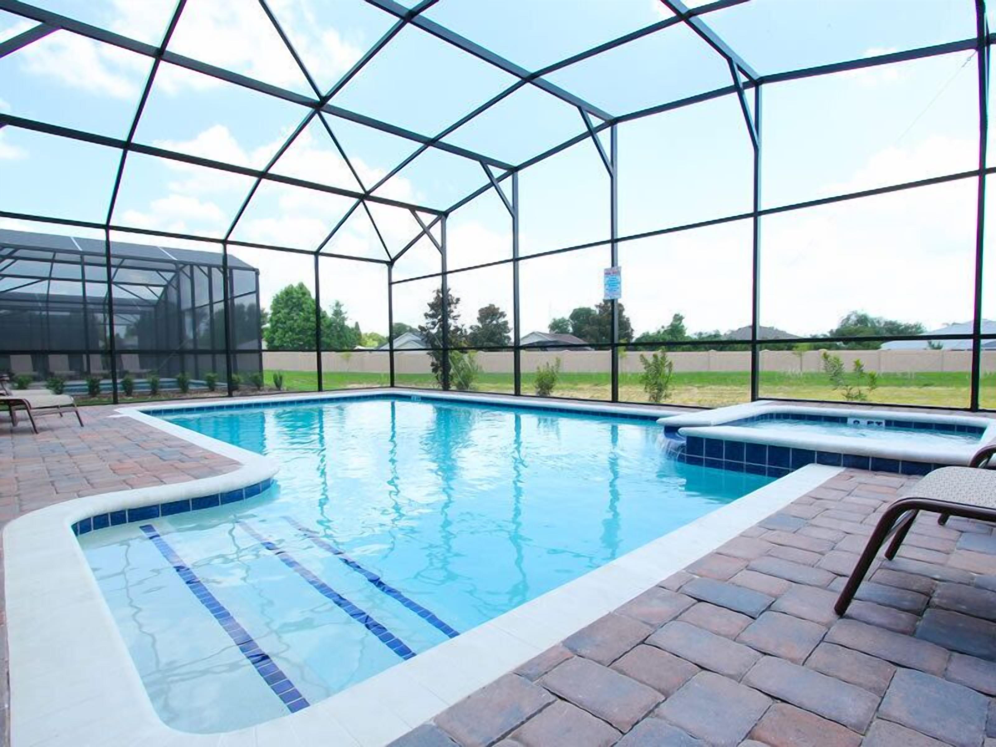 A covered swimming pool with a hot tub, surrounded by a glass enclosure, and a brick patio area.