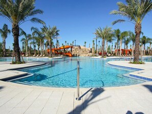 Una piscina con tobogán de agua, rodeada de palmeras y sillas de descanso.