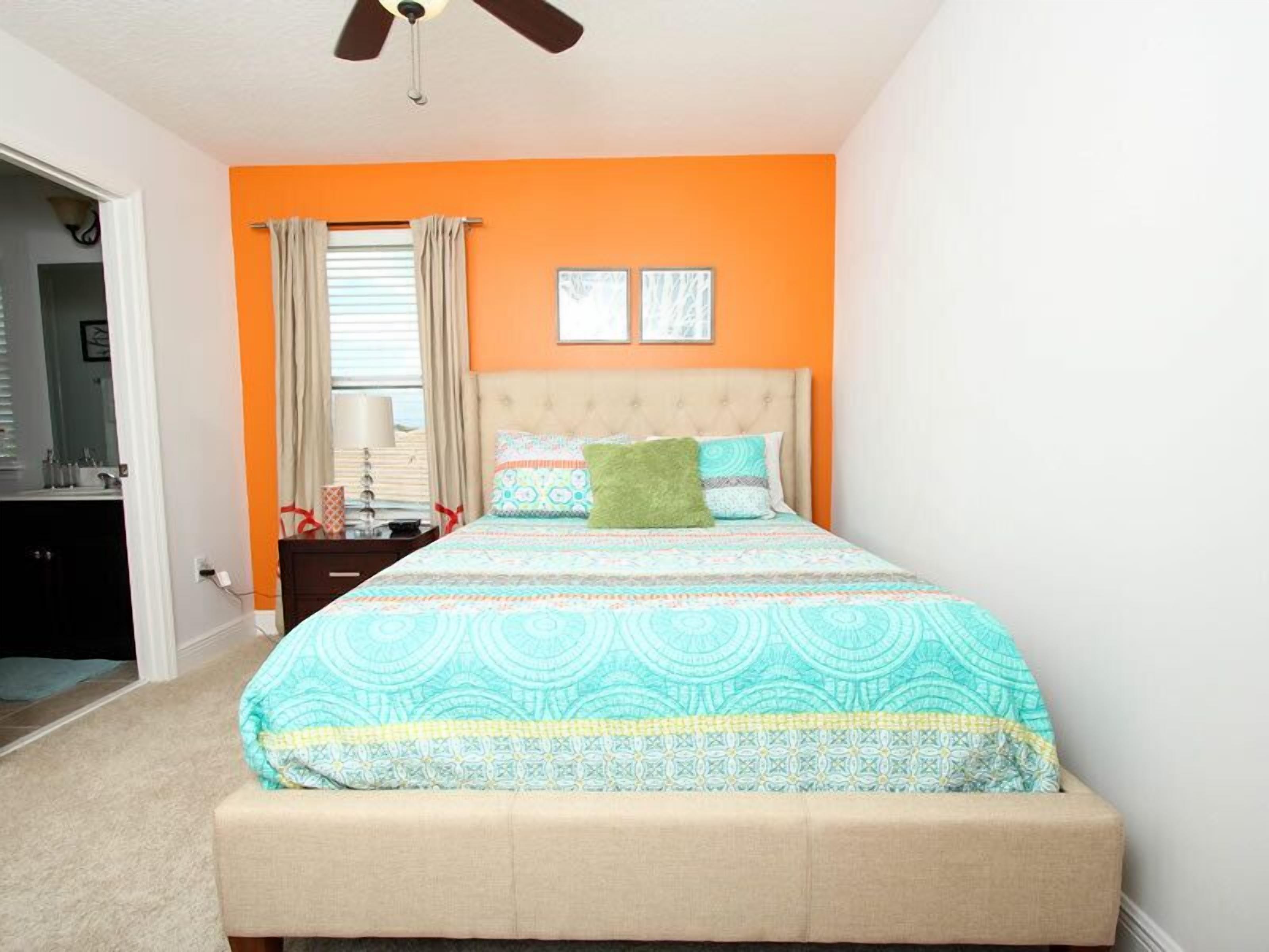 A bedroom with a bed, a nightstand, a window with curtains, and a ceiling fan.
