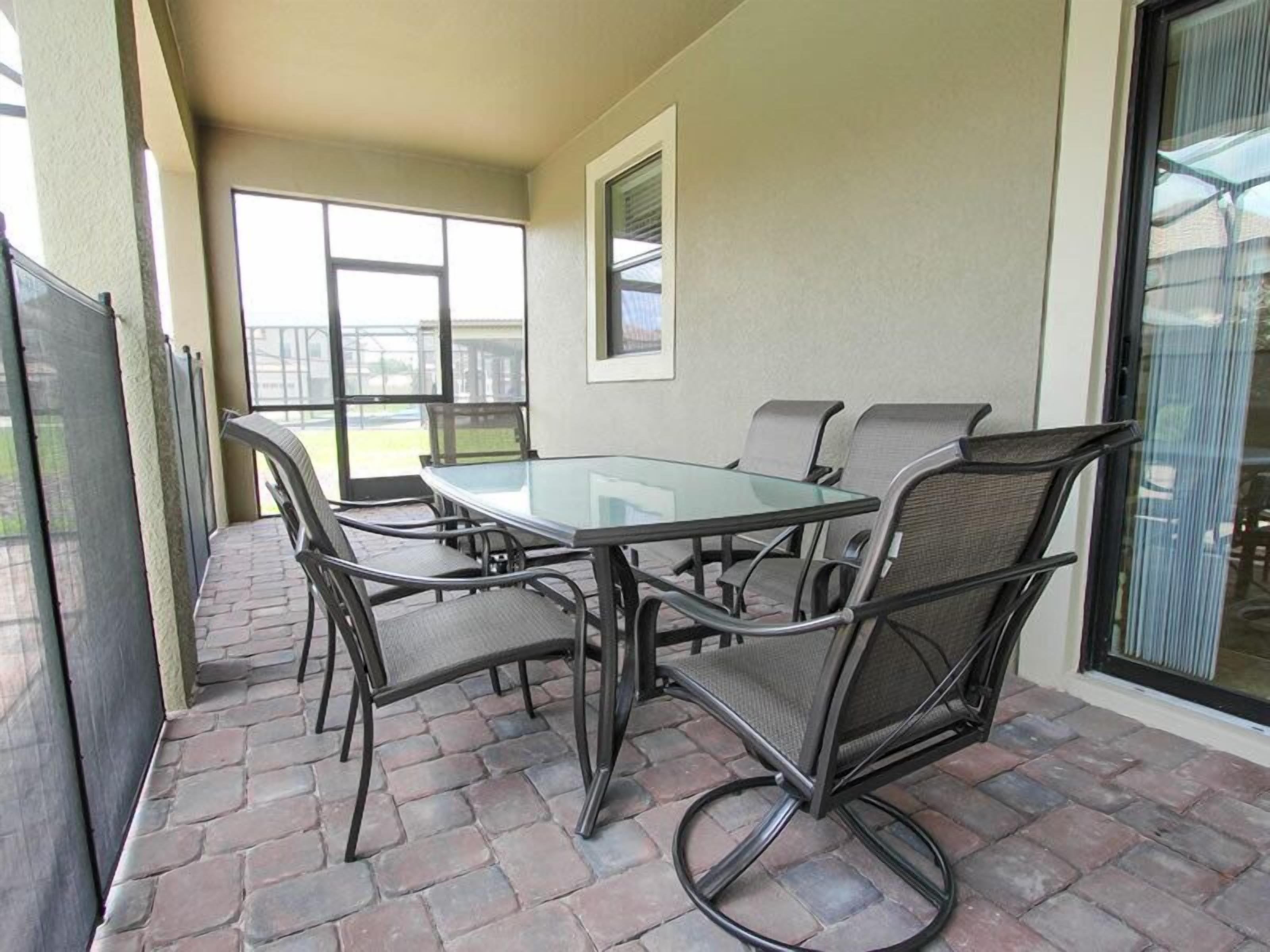 Un patio exterior con una mesa de vidrio y sillas de metal.