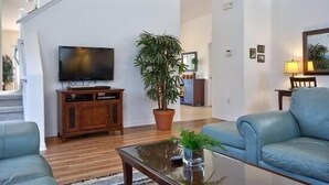 A modern living room with a flat-screen TV, a wooden entertainment unit, a large potted plant, and two blue leather sofas.