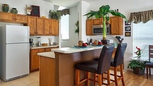 A modern kitchen with wooden cabinets, a white refrigerator, a central island with bar stools, and a microwave.
