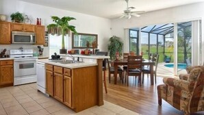 A modern kitchen with wooden cabinets, a central island, and a dining area with a view of a swimming pool.