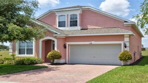 A single-story house with a pink exterior, a white garage door, and a brick driveway.