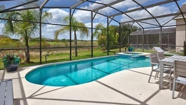 A covered outdoor swimming pool with a view of palm trees and a clear sky.