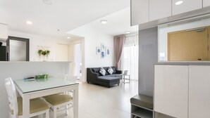 Una cocina moderna con armarios blancos, una mesa de comedor de vidrio y un sofá gris.