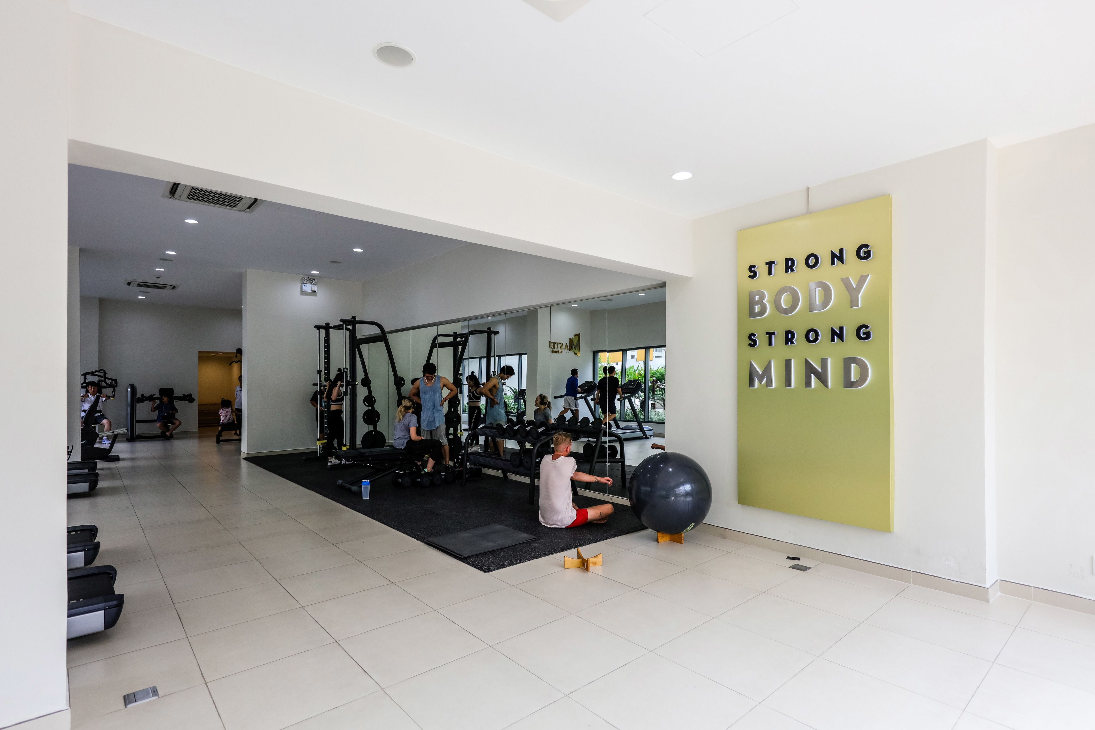 Un gimnasio con diferentes equipos de ejercicio, una frase motivacional en la pared y un espejo que refleja el espacio.