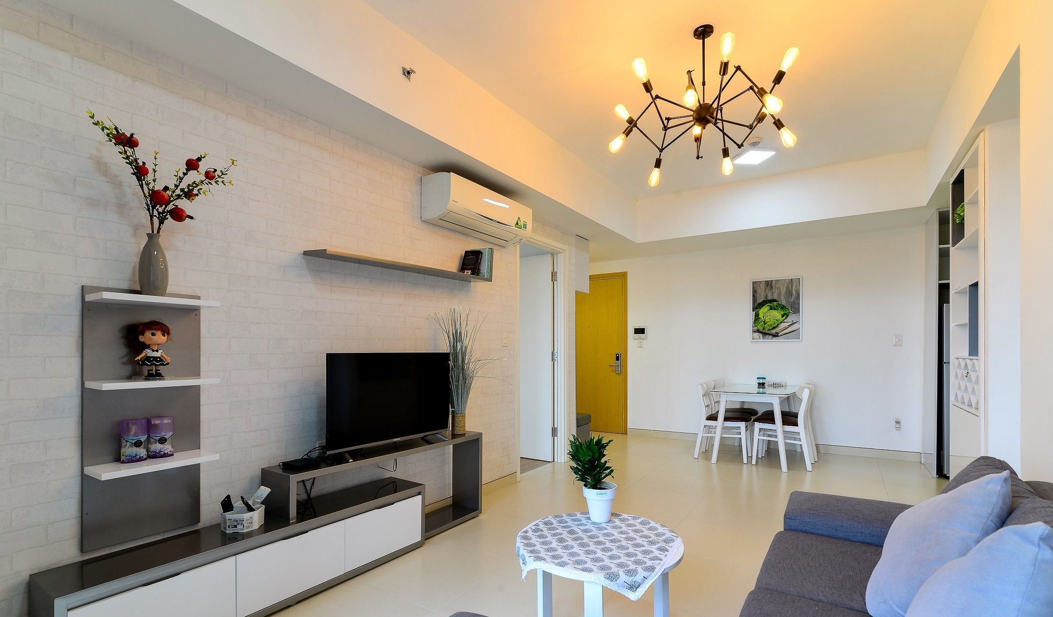 A modern living room with a flat-screen TV, a dining area with a table and chairs, and a staircase leading to another level.
