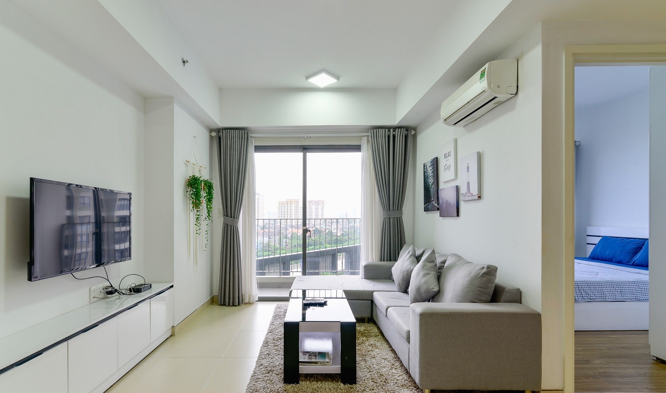 A modern living room with a flat-screen TV, a sofa, a coffee table, and a balcony with curtains.