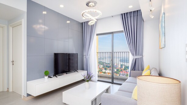 Una sala de estar moderna con un televisor de pantalla plana, una mesa de centro blanca, un sofá y un ventanal con vistas a la ciudad.