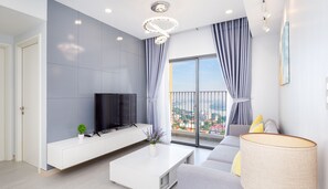 A modern living room with a flat-screen TV, a white coffee table, a sofa, and a large window with a city view. - MRT Apartment in Masteri Thao Dien (Ho Chi Minh City)