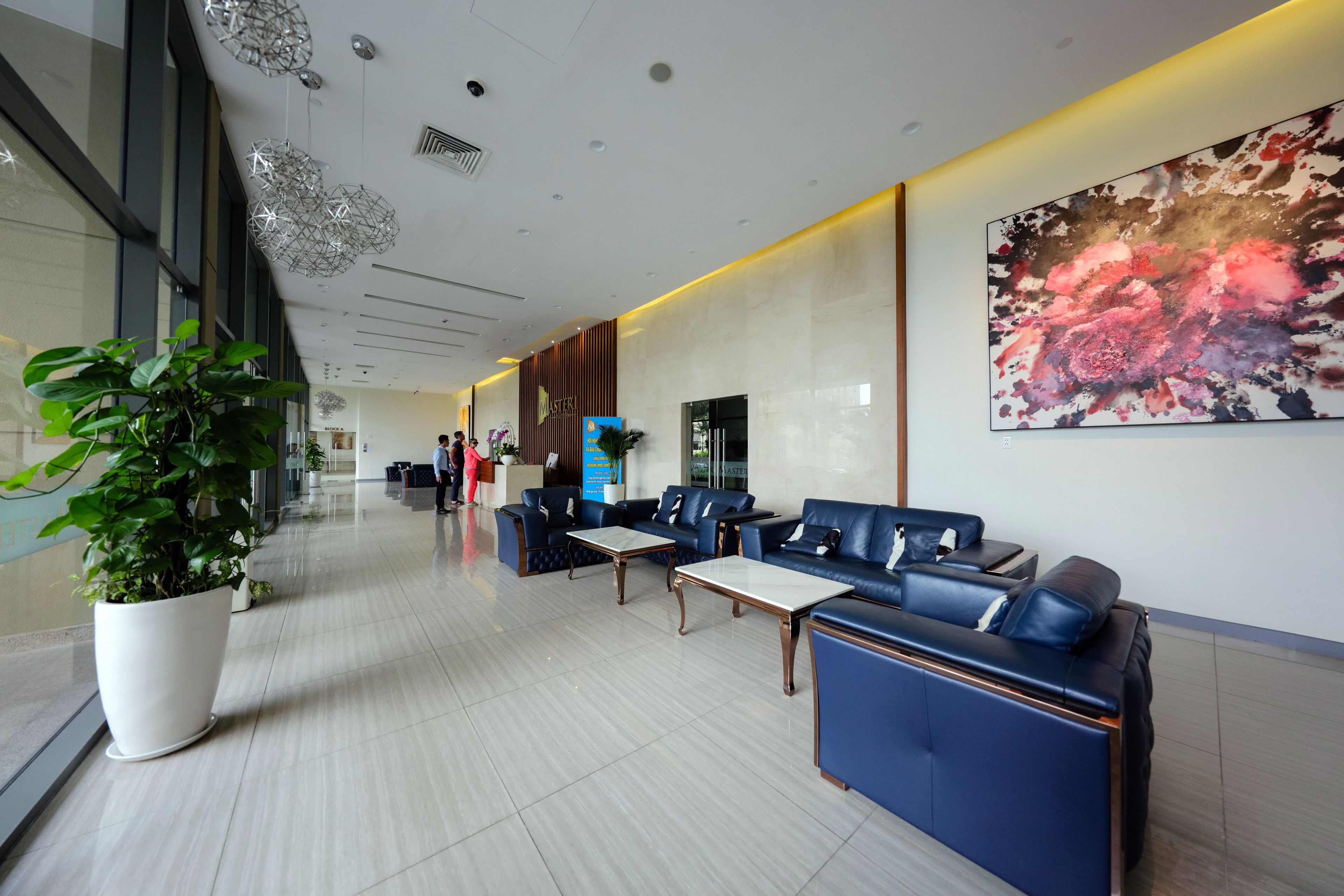 A modern hotel lobby with a seating area, a large potted plant, and a wall-mounted artwork.