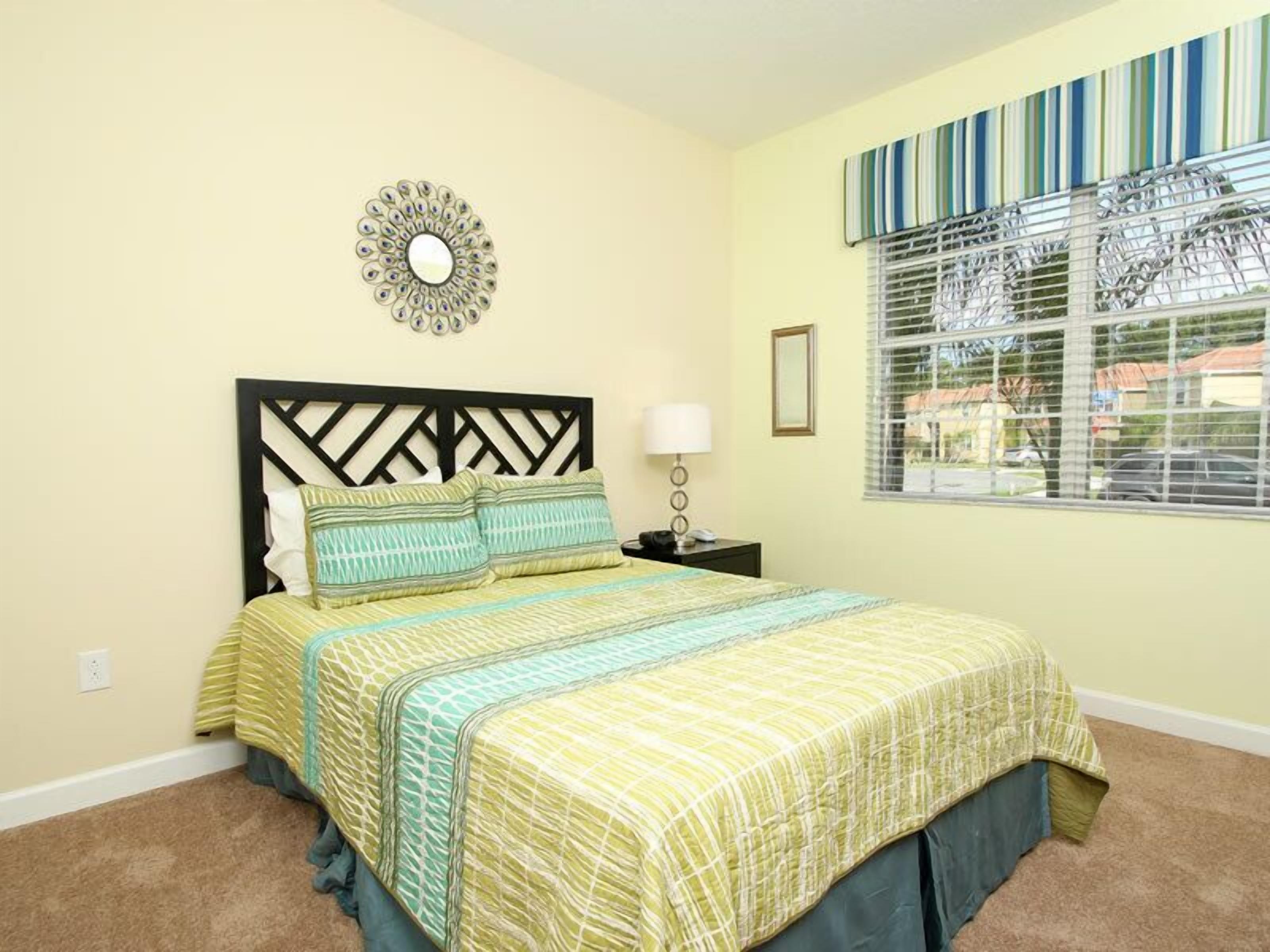 A bedroom with a bed, a nightstand, a lamp, a wall decoration, and a window with blinds.