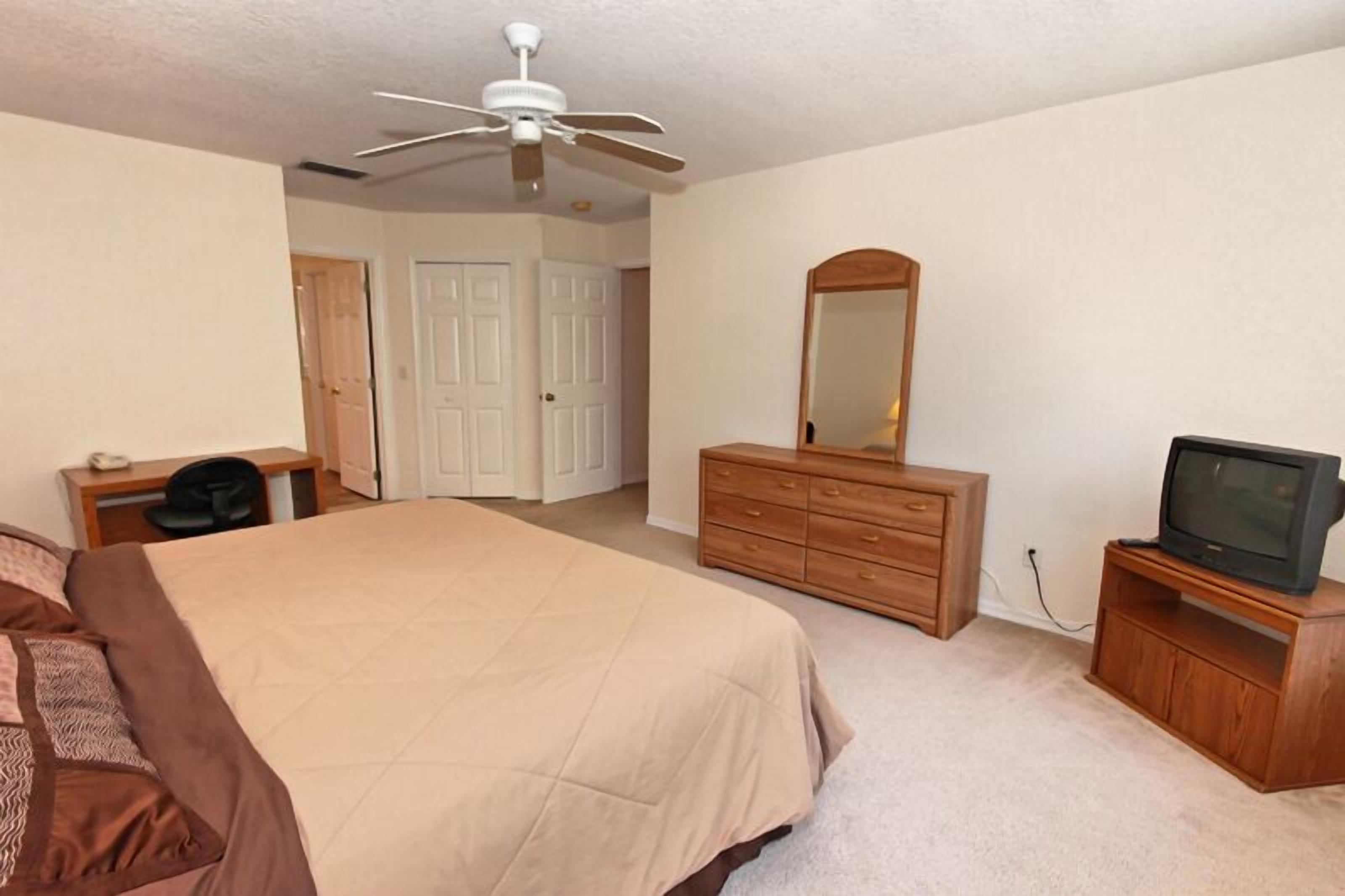A bedroom with a bed, a dresser, a television, and a ceiling fan.