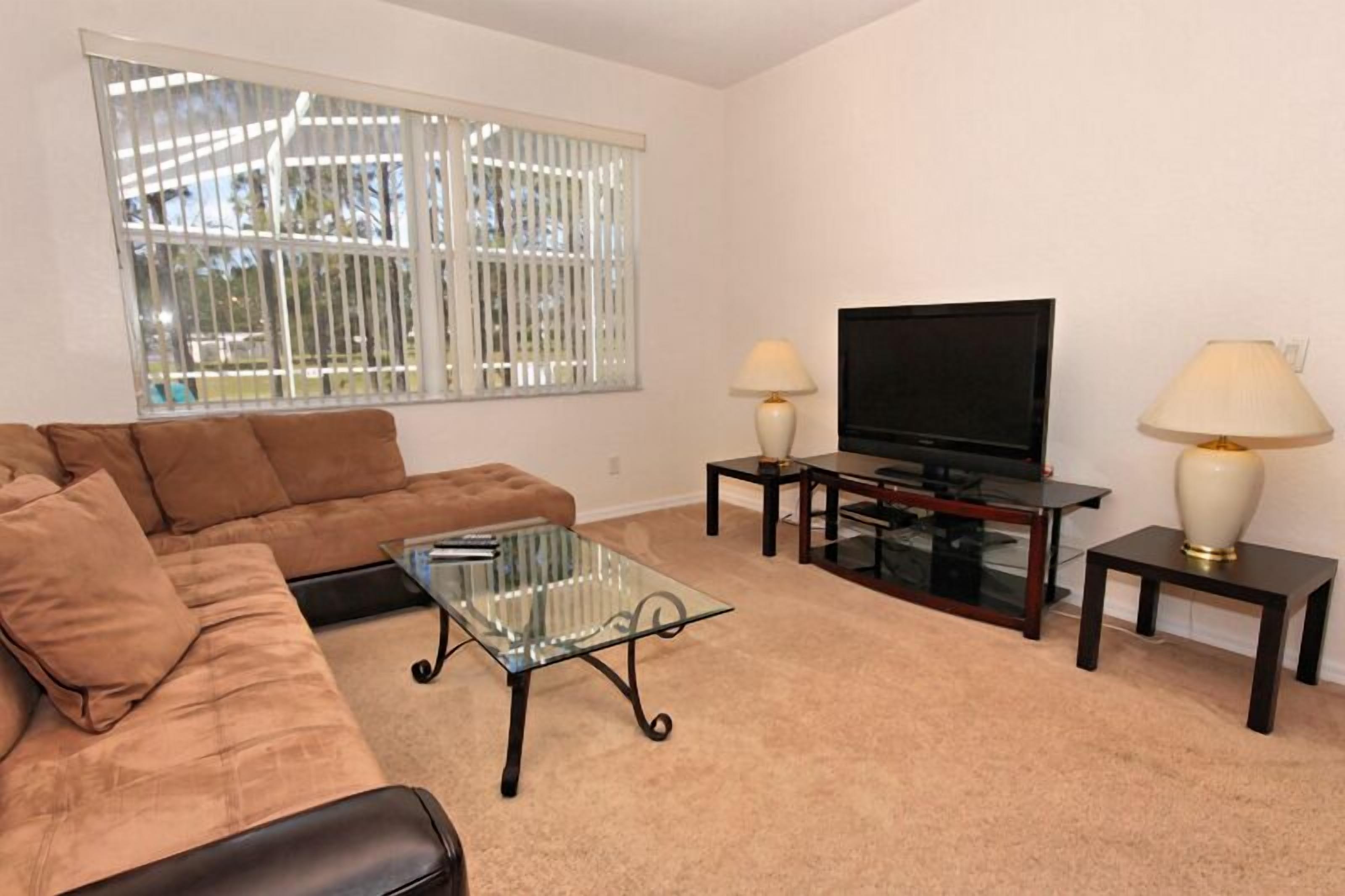 A living room with a brown sofa, glass coffee table, TV, and two lamps on side tables.